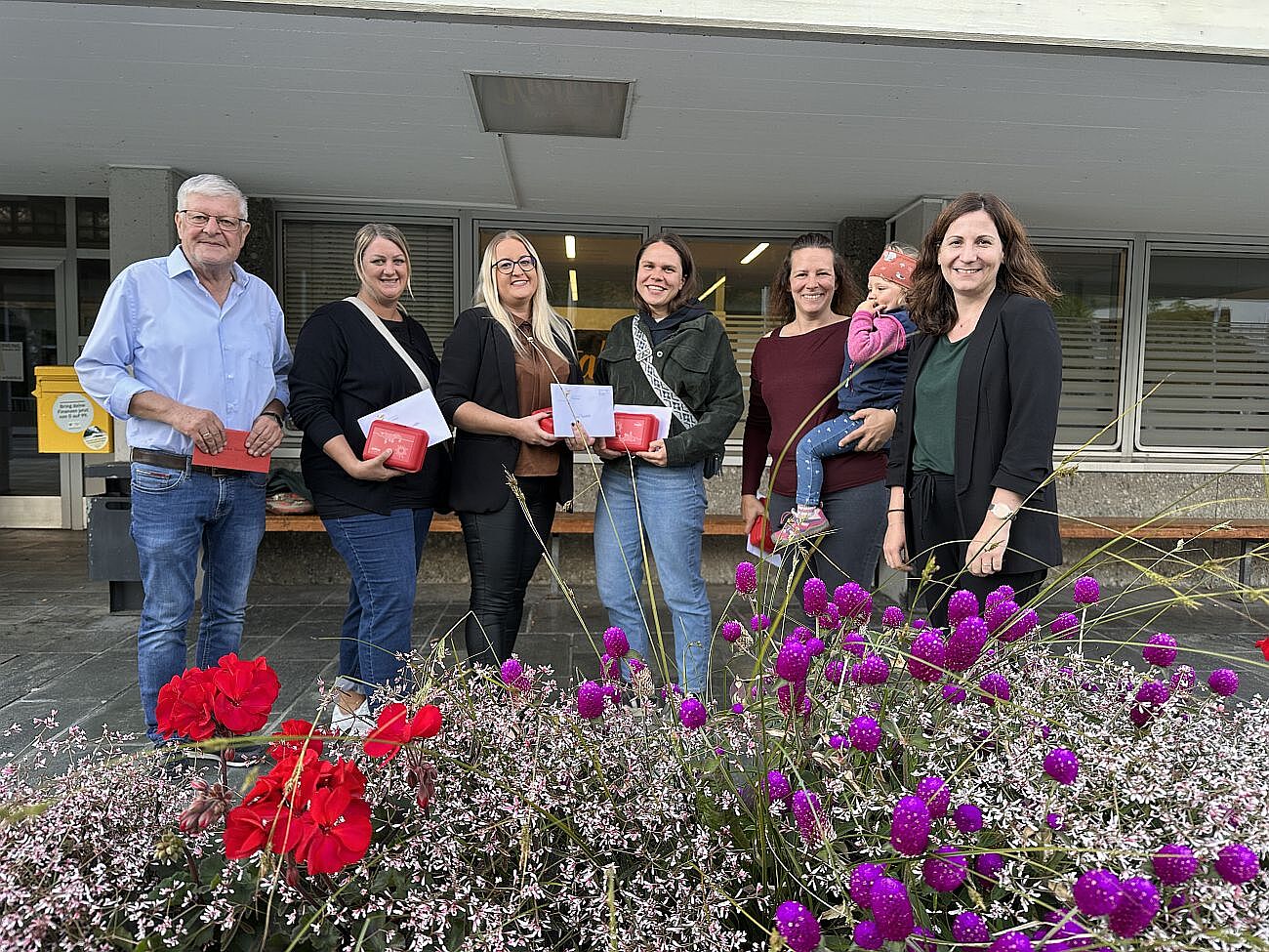 Sechs Personen mit roten Geschenken vor einem Gebäude in Österreich