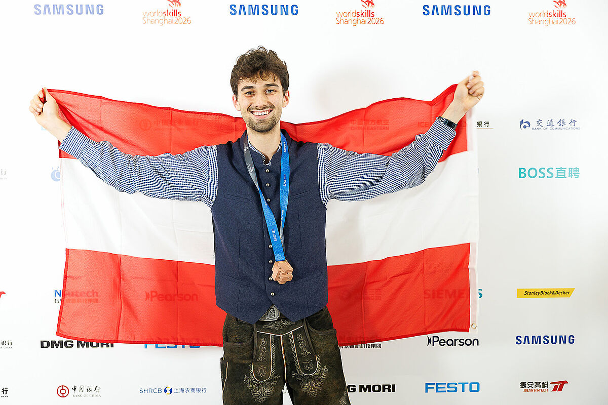 Rene Bitschnau hat die Bronze-Medaille umgehängt und hält die Österreich-Fahne. (Fotoquelle: SkillsAustria-Wieser-Slovencik)