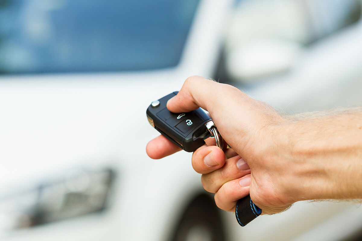 Person drückt beim Autoschlüssel auf den Knopf, um das Fahrzeug im Hintergrund abzusperren. (Fotoquelle: iStock/denkcreative)